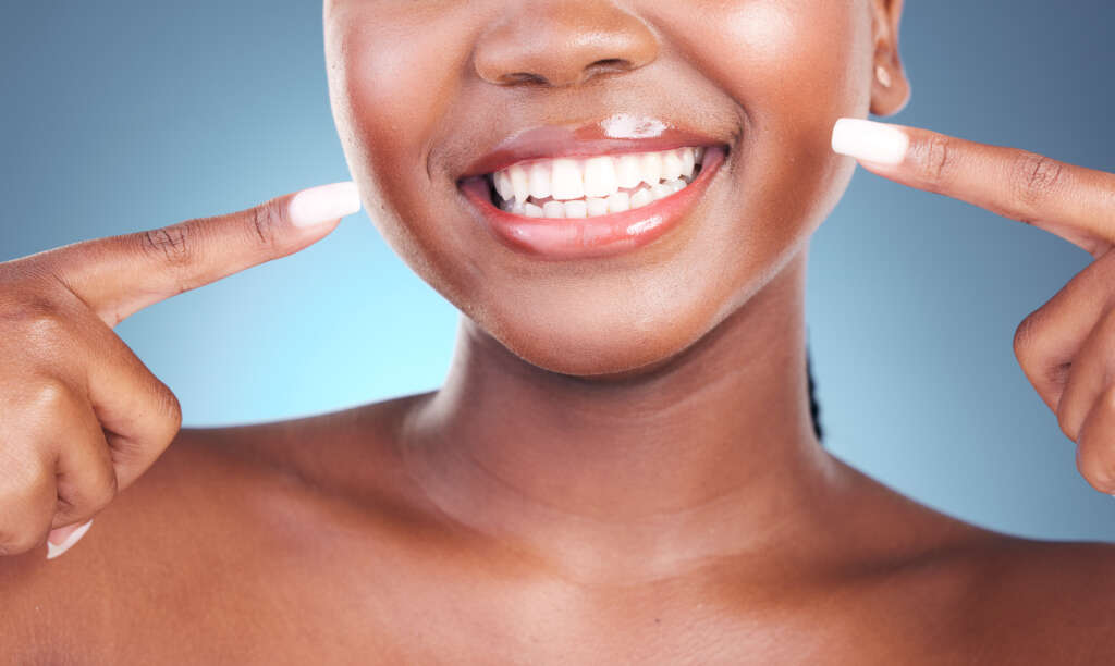 Happy woman, teeth and pointing in dental cleaning, hygiene or treatment against a blue studio back.